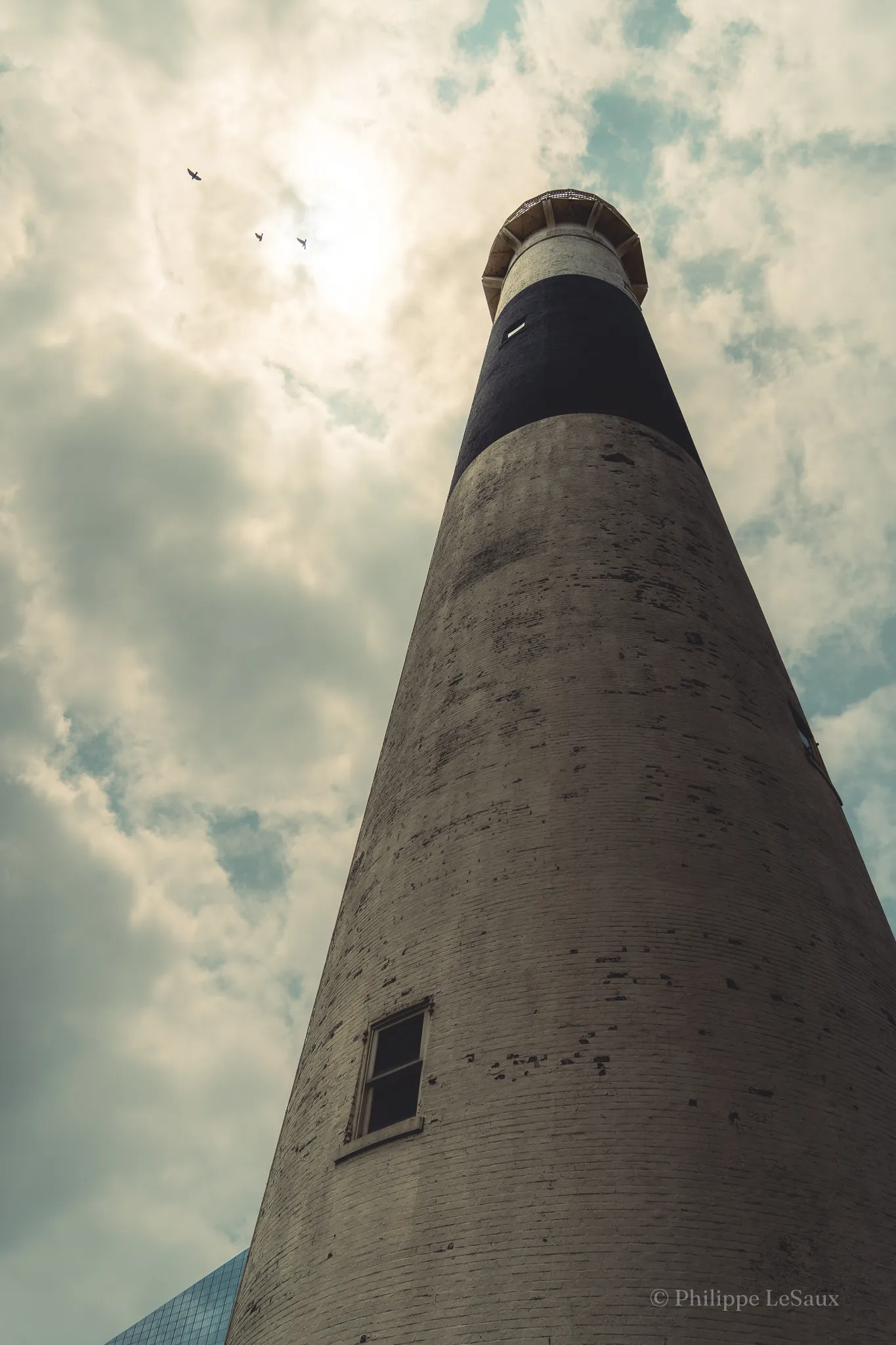 Looking up at a lighthouse tower with birds circling overhead under dramatic clouds