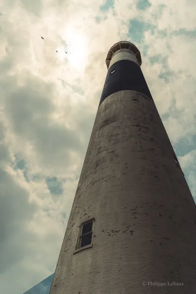 Looking up at a lighthouse tower with birds circling overhead under dramatic clouds