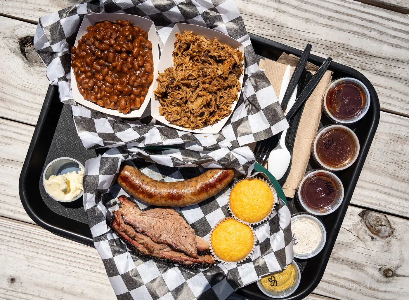 A tray of barbecue with brisket, sausage, pulled pork, beans, and cornbread