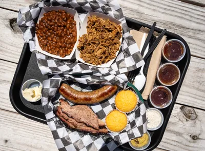 A tray of barbecue with brisket, sausage, pulled pork, beans, and cornbread