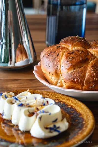 A braided herbed bread loaf beside flower-garnished butter pats on a wooden table