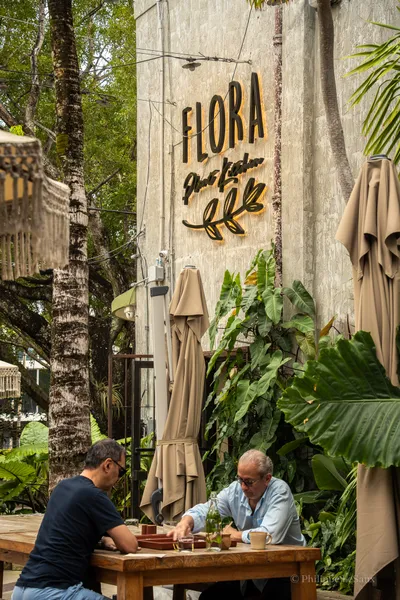 Two diners at an outdoor table beneath the Flora Plant Kitchen sign