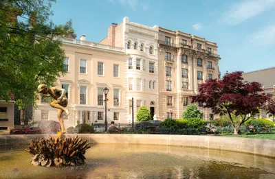 A neoclassical mansion viewed across an ornamental fountain with colorful trees
