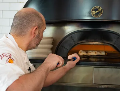 A chef tends to food inside a Moretti wood-fired oven